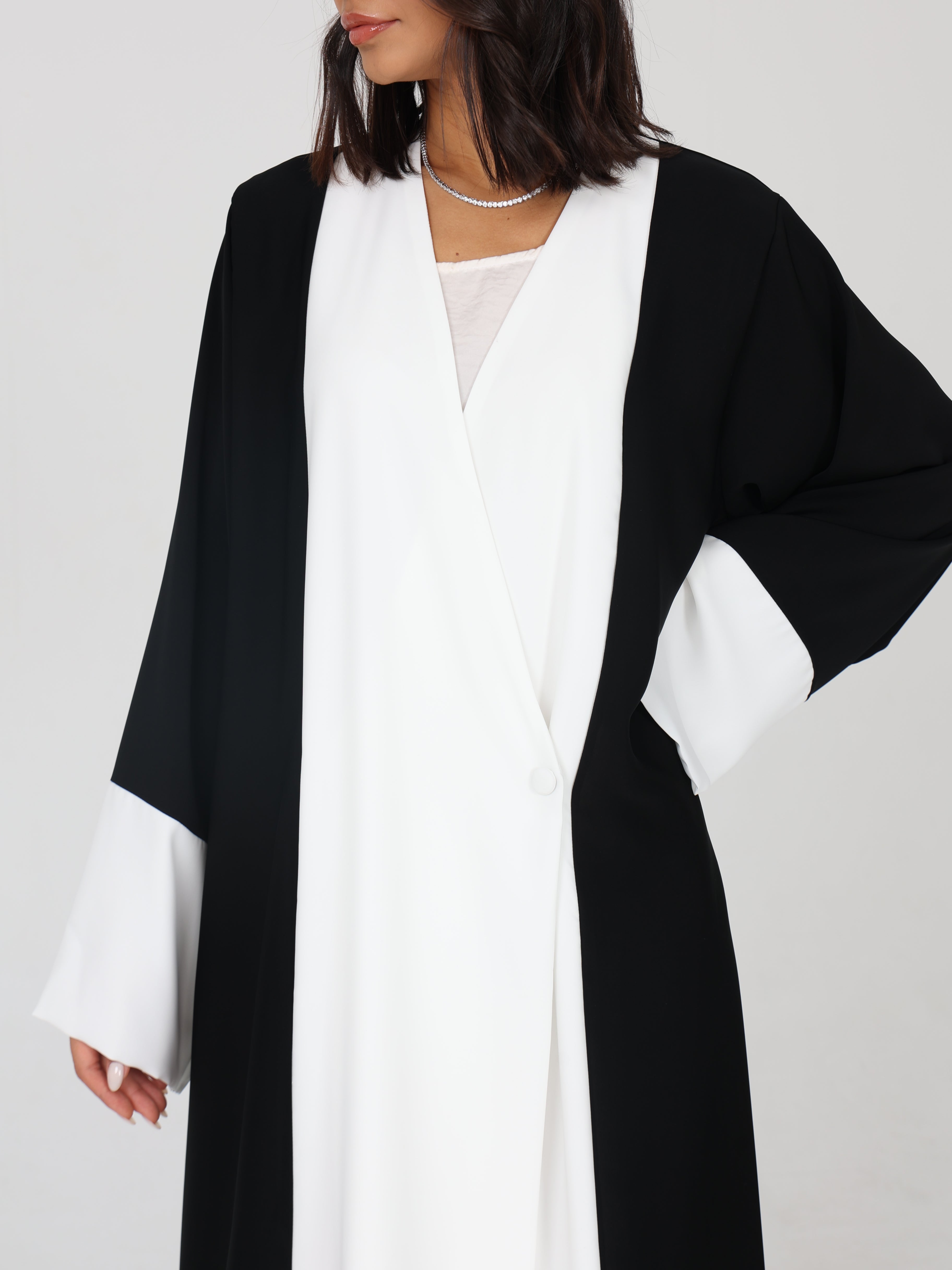 Close-up of RUMI abaya with black sleeves, white front panel, tux like and a single side button