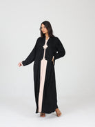 Model posing in black RUMI abaya with beige panel and decorative square buttons