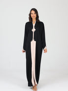 Model walking forward in black RUMI abaya with beige accents and square buttons, white background