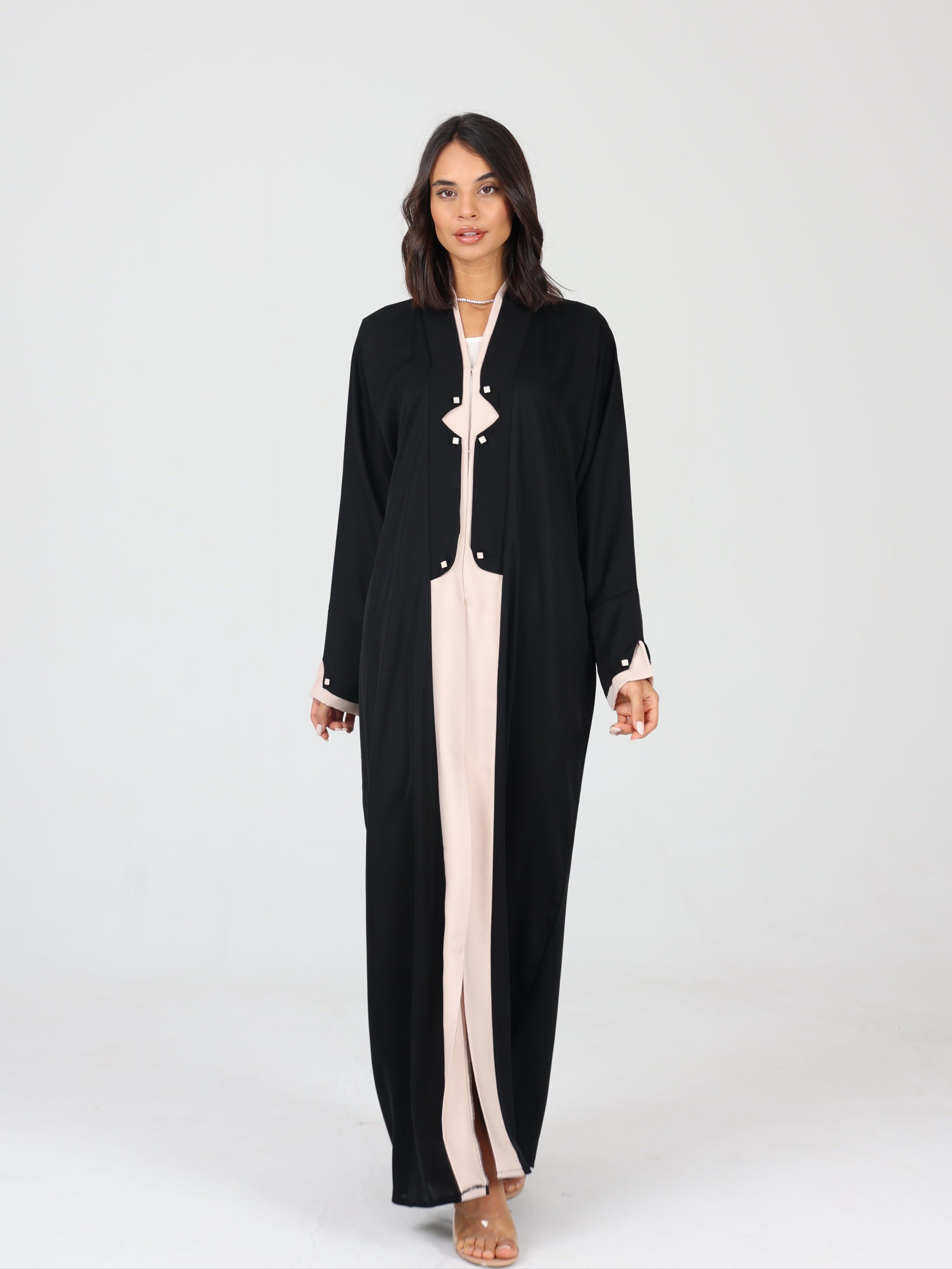 Model walking forward in black RUMI abaya with beige accents and square buttons, white background