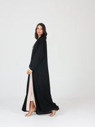 Side view of model walking in black RUMI abaya with flowing beige trim and soft fabric
