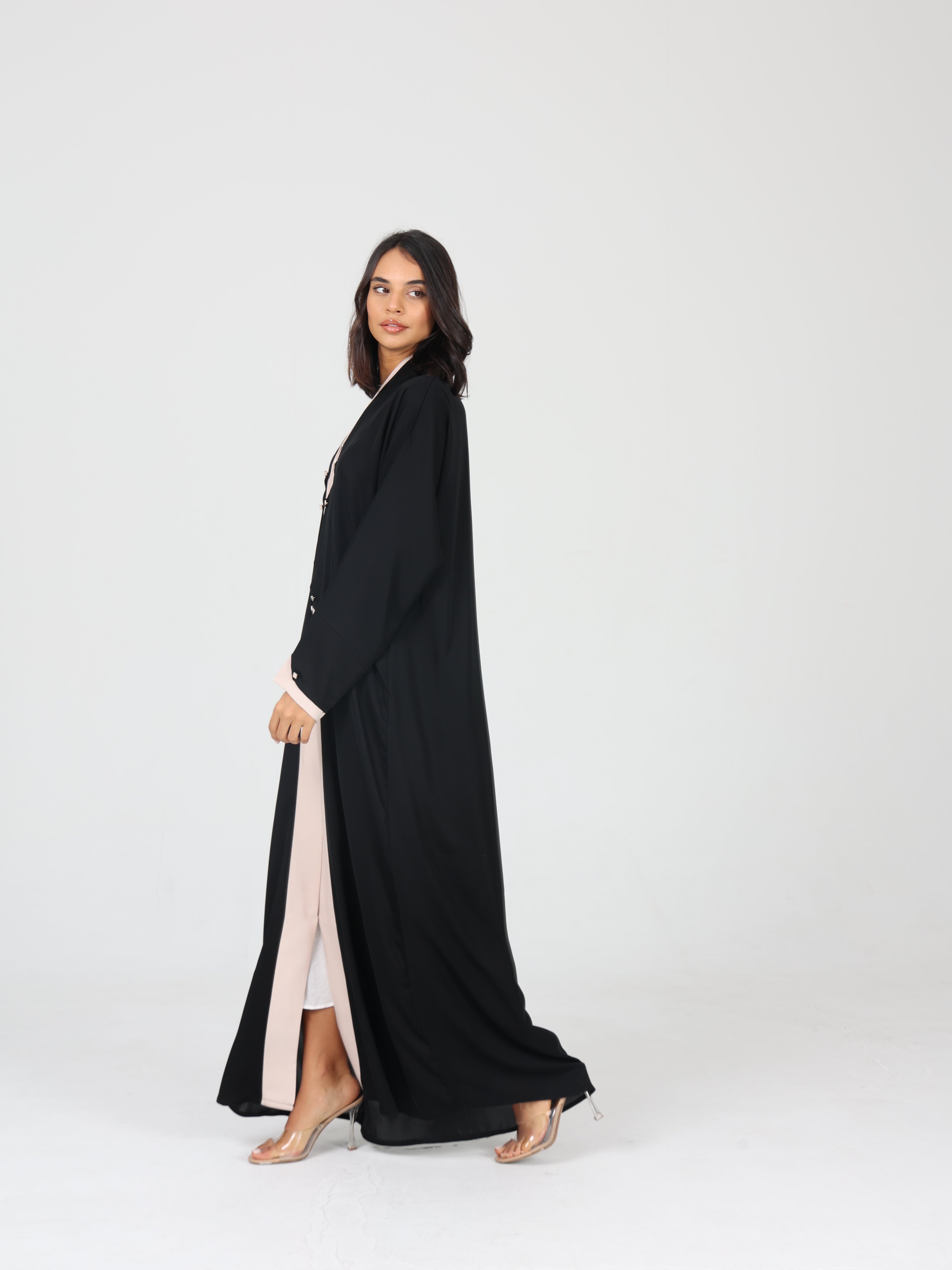 Side view of model walking in black RUMI abaya with flowing beige trim and soft fabric