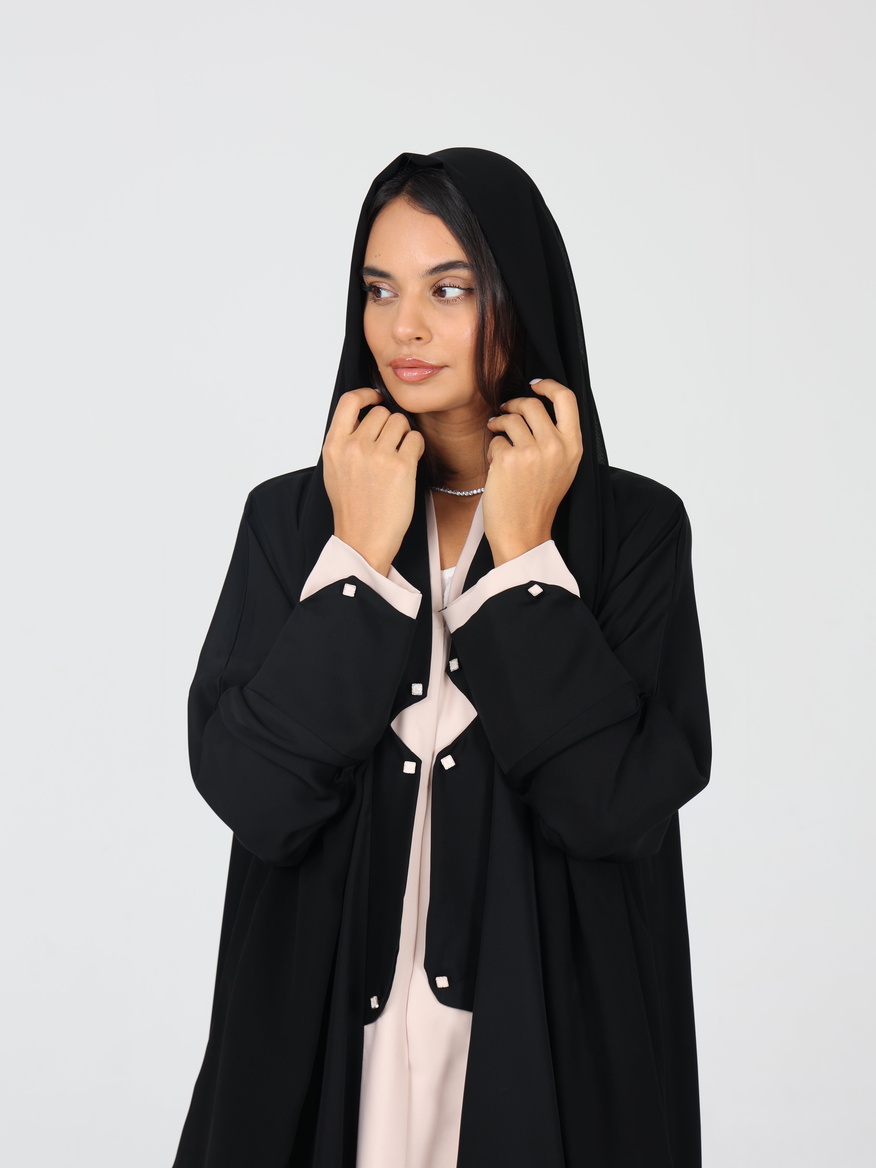 Model holding up black shaila RUMI abaya with beige details and button accents