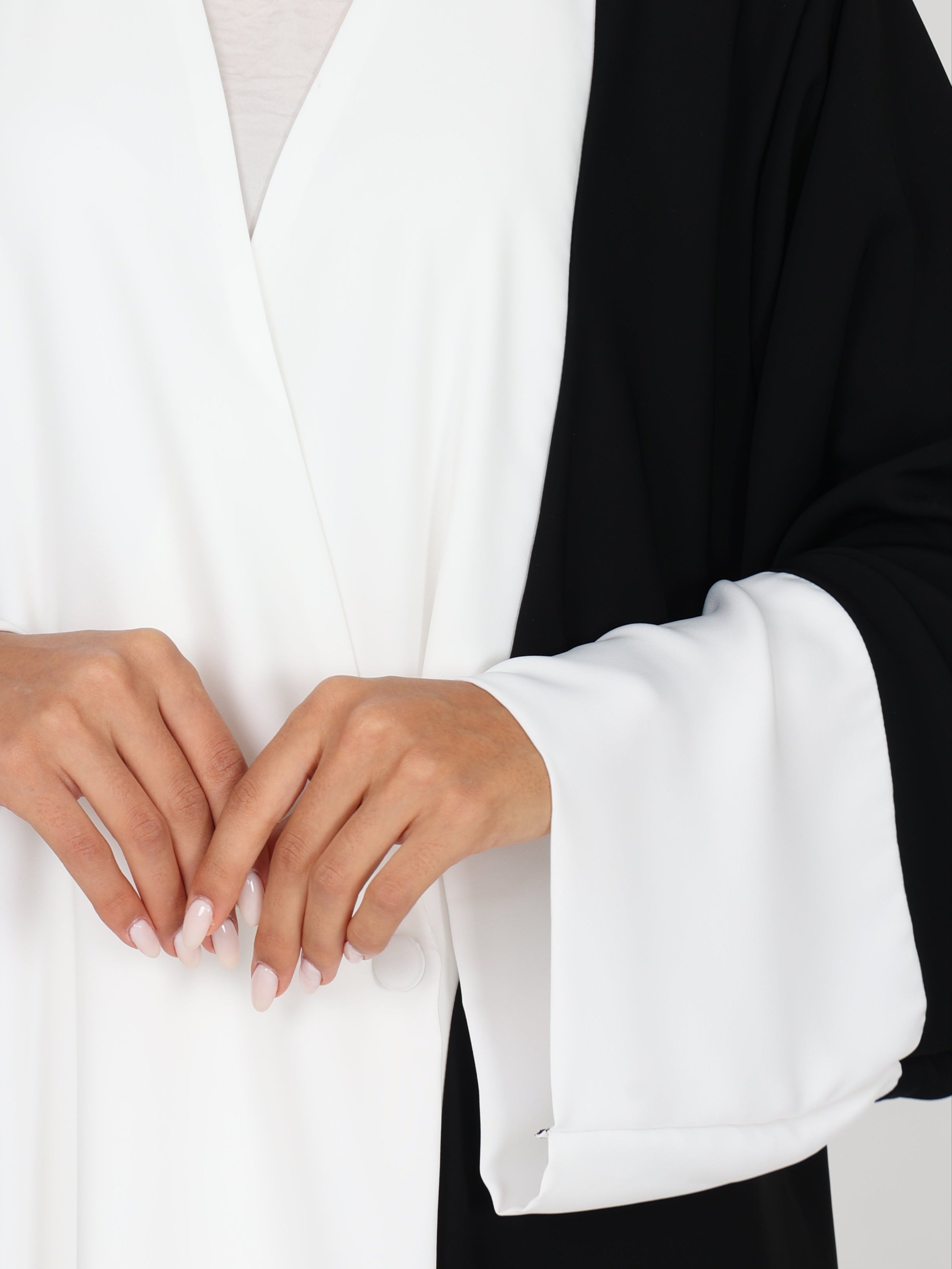 Close-up of RUMI abaya sleeves and hands, showing smooth white fabric and subtle button closure