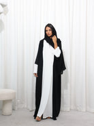 Model wearing black and white RUMI abaya with black sheila , standing in front of a white curtain backdrop