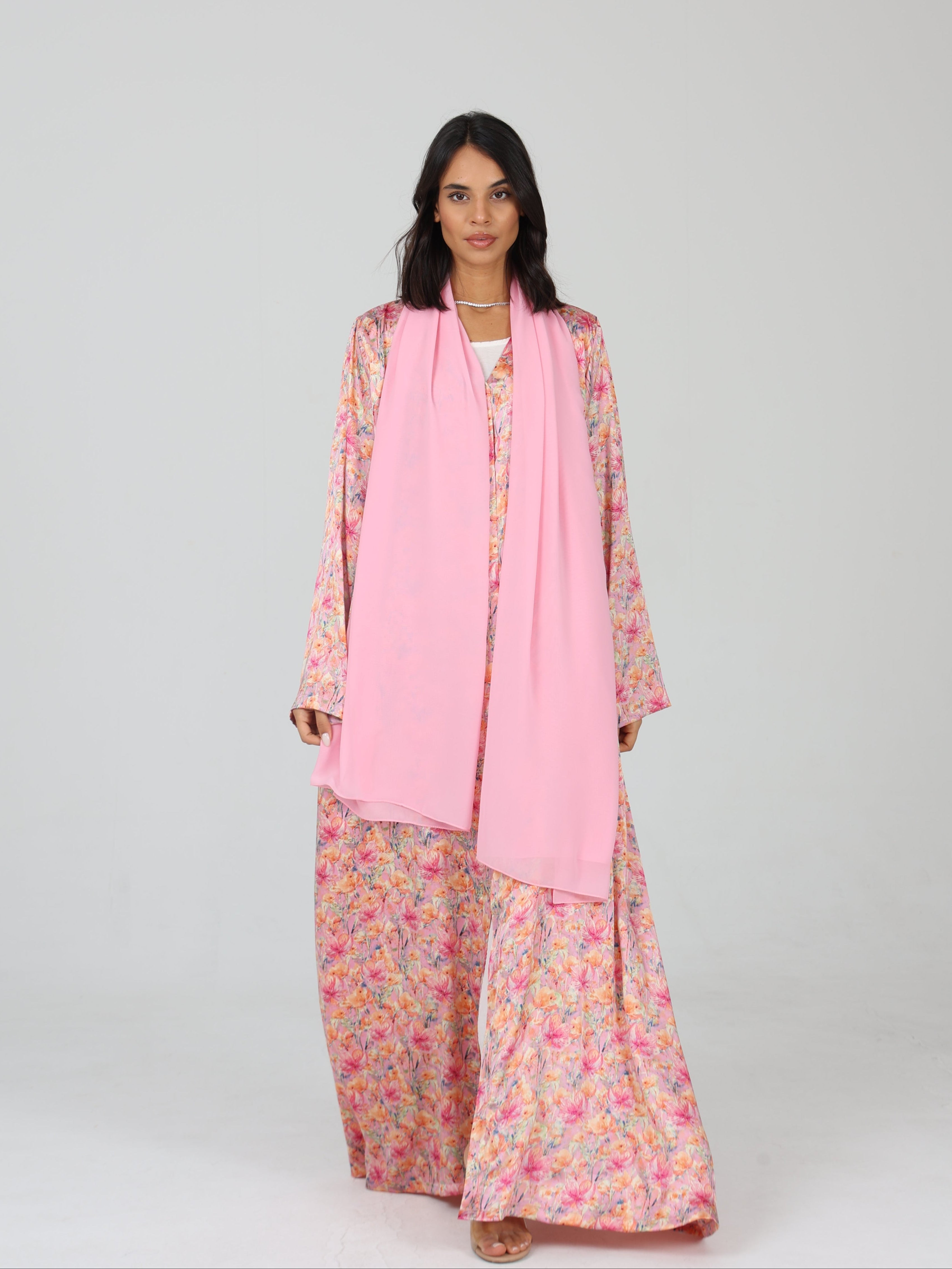 Model walking forward in RUMI pink floral abaya with soft chiffon scarf and relaxed silhouette