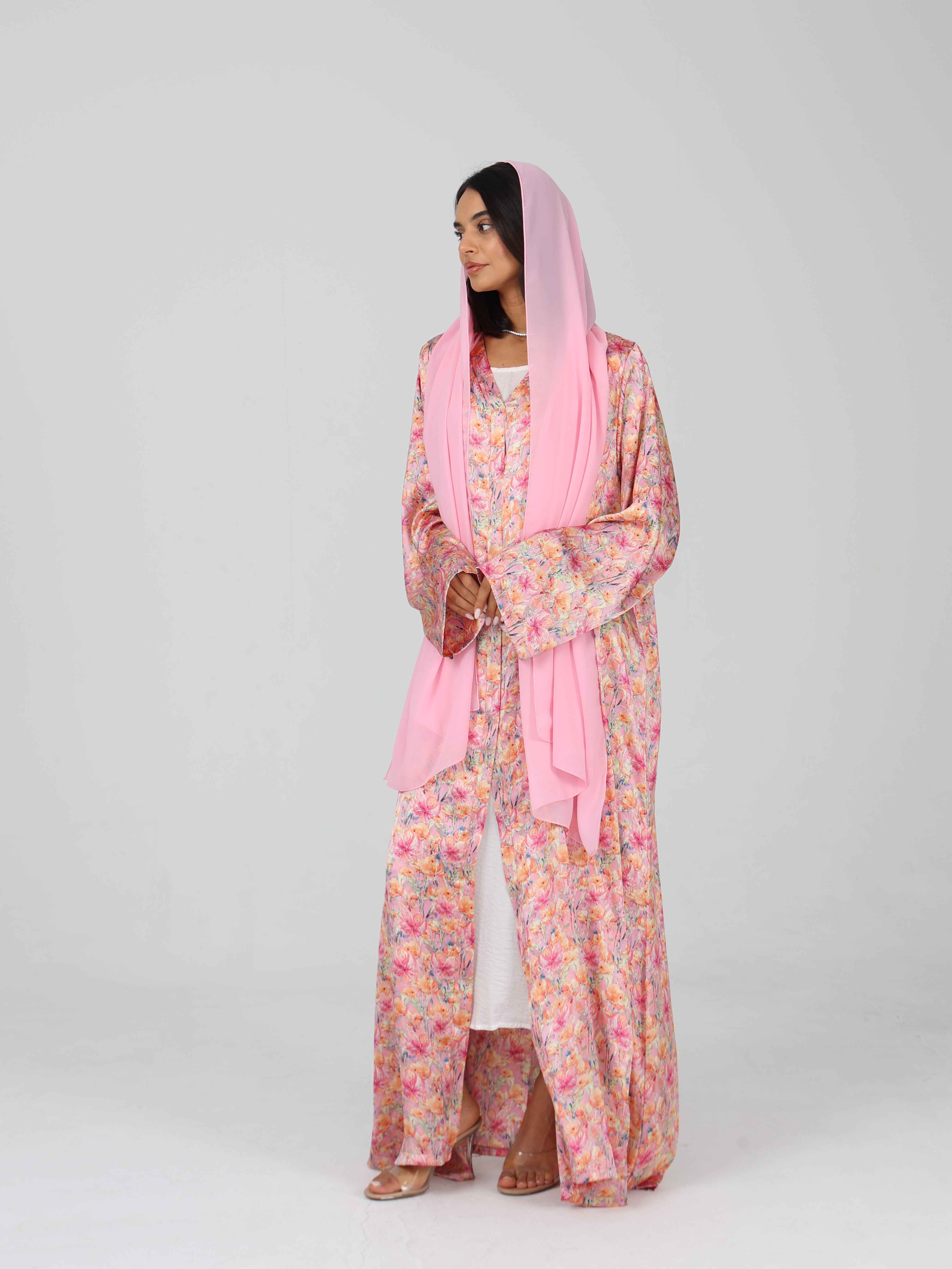 Side view of model in RUMI pink floral abaya with pink sheila scarf, showing front pleats and sleeves