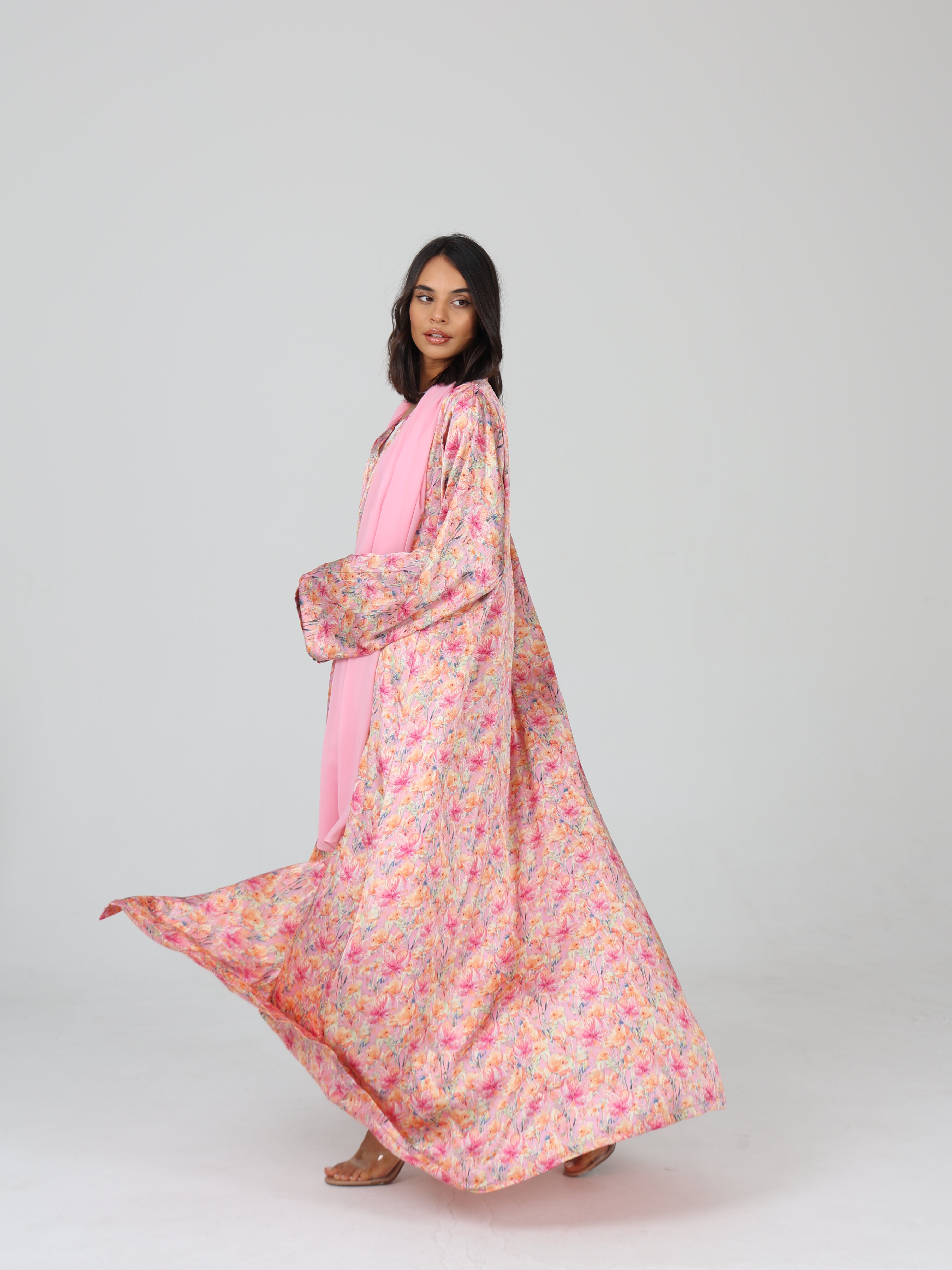 Model in RUMI pink floral abaya mid-turn, showing the fabric’s flow and full print in motion